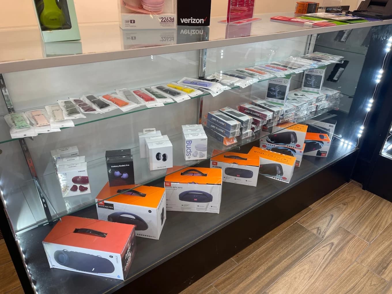 Glass retail display case showcasing colorful watch bands, portable speakers, and wireless earbud packaging.