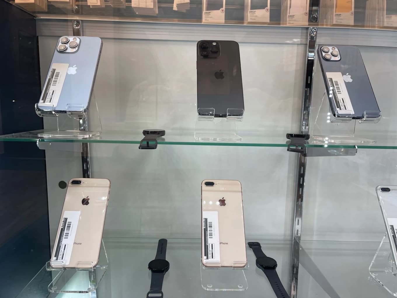 Various iPhones and black smartwatches displayed on glass shelves in a retail store showcase.